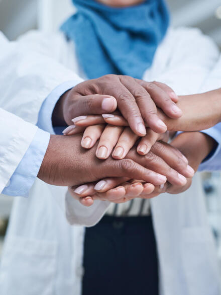 Shot of a group of unrecognisable scientists joining hands in solidarity in a laboratory.